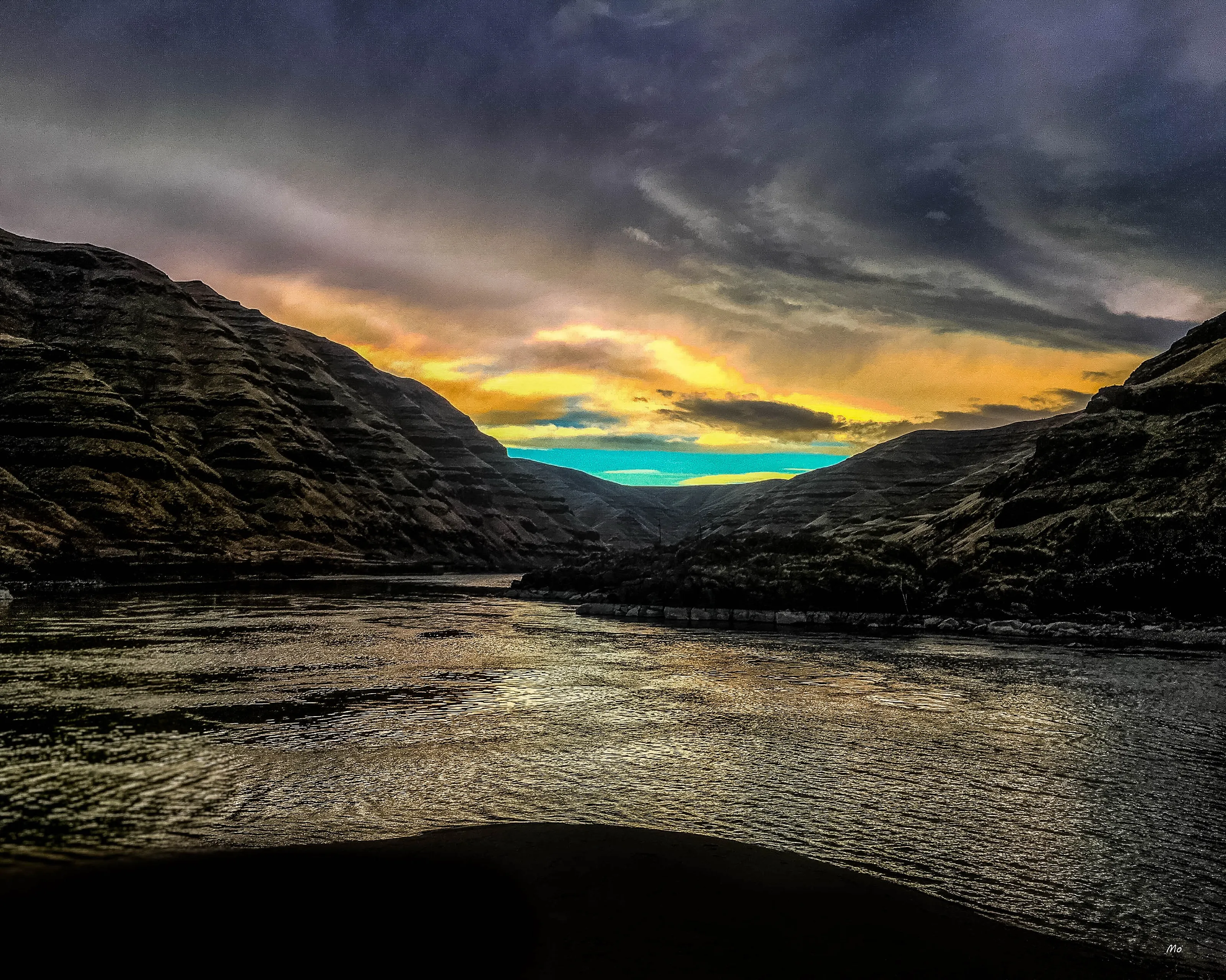 A dark canyon river at sunset under a gold and teal sky