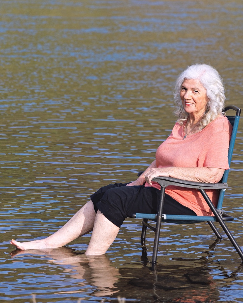 Maureen Weber, seated in a camp chair at the edge of a river